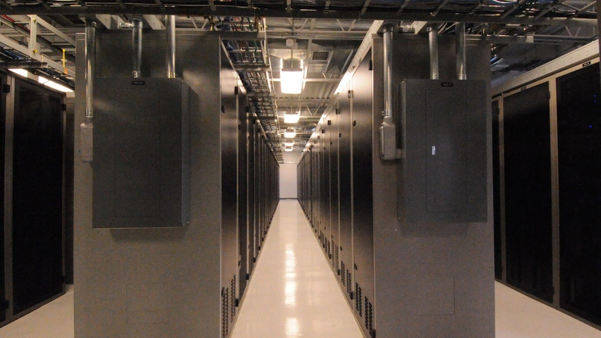 Pasillo de un centro de datos con filas de gabinetes y tuberías superiores